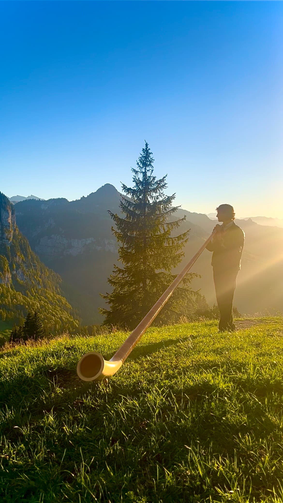 Ruben spielt Alphorn auf einer Bergwiese im Abendlicht